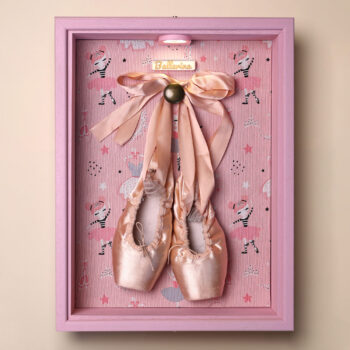 Caja para puntas de ballet Clara vista de frente, con marco rosa lacado, fondo de bailarinas e iluminación LED encendida